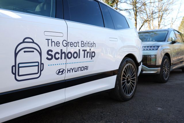 White car with branding reading 'The Great British School Trip' and a Hyundai logo, parked beside another vehicle.