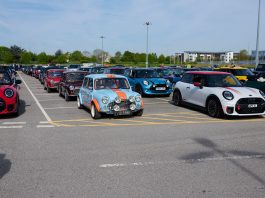 Line of colourful classic Mini cars parked in a lot during a car show/meetup.