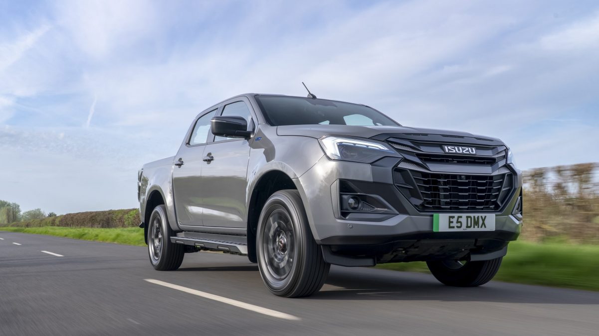 The new Isuzu d-max ev-cross Gray Isuzu pickup truck in motion on a two-lane road under a blue sky, from a low-angle side view.