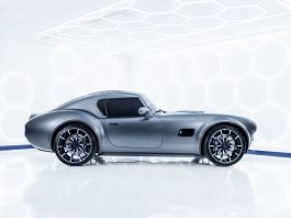 Side view of a sleek grey/blue sports car in a bright white showroom with hexagonal LED wall panels.