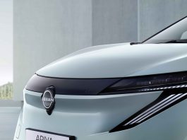 Close-up of a light-blue Nissan Ariya's front end, showing the emblem, sleek headlight, and smooth hood.