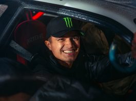 Smiling man wearing a black cap with a green Monster logo inside a car.