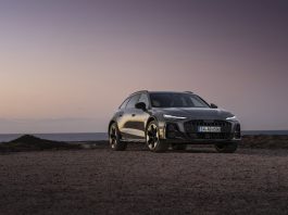 Silver Audi SUV parked on a rocky coastal shore at sunset with calm water in the background.