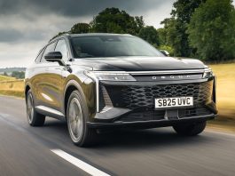 Front three-quarter view of a silver SUV speeding along a rural highway with blurred road and green fields in the background.