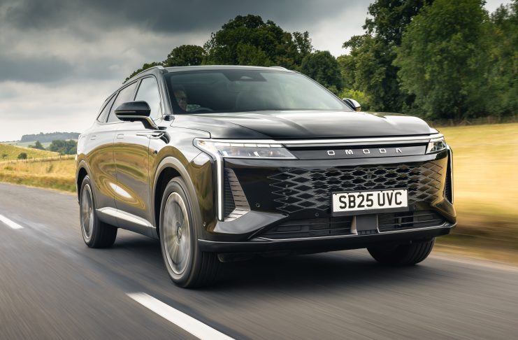 Front three-quarter view of a silver SUV speeding along a rural highway with blurred road and green fields in the background.