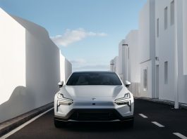 Front view of a white car parked in a narrow alley between tall white buildings under a blue sky.