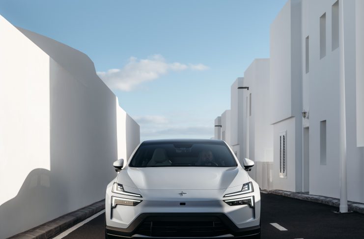 Front view of a white car parked in a narrow alley between tall white buildings under a blue sky.