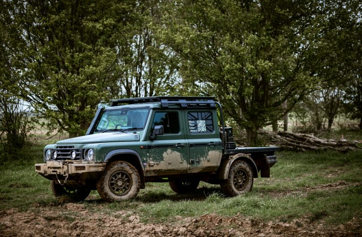 Green 4x4 SUV with a roof rack parked in a muddy field, with dense trees in the background.